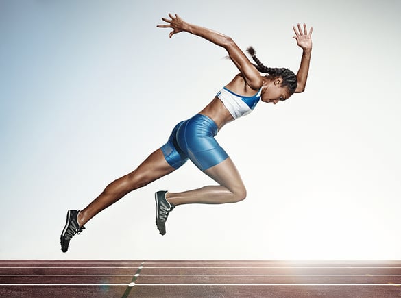 Woman in running form about to take off running on an outdoor track.